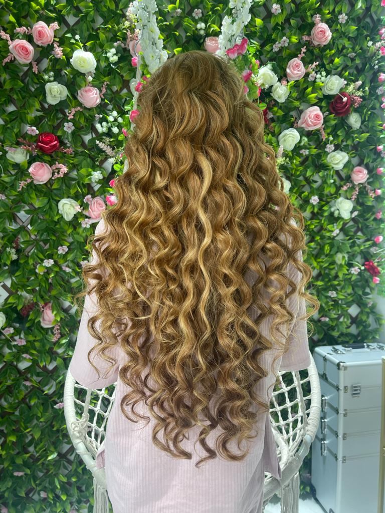 Long golden curls styled at Bellaliza Salon in front of a flower wall